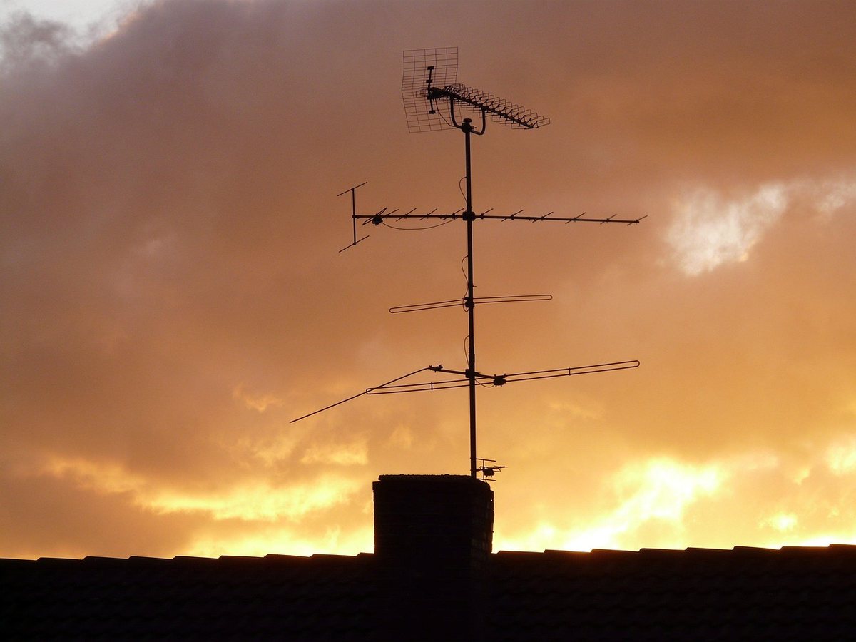 Antenne TV silhouette sur cheminée, ciel orange crépusculaire