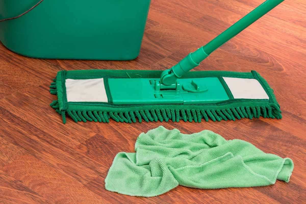 Balai vert posé sur un sol en bois avec un chiffon et un seau à proximité