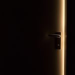 Une porte sombre avec poignée, lumière dorée perçant l'obscurité