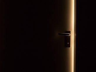 Une porte sombre avec poignée, lumière dorée perçant l'obscurité