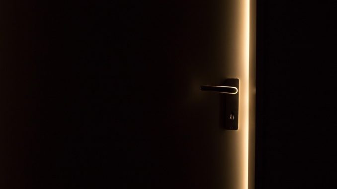 Une porte sombre avec poignée, lumière dorée perçant l'obscurité