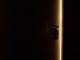 Une porte sombre avec poignée, lumière dorée perçant l'obscurité